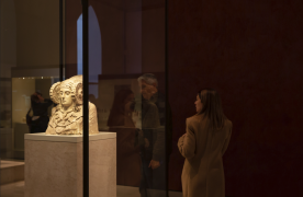 Dama de Elche en una vitrina y dos visitantes que la observan desde la izquierda