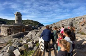 Vista del far de sa Creu amb un grup de persones en una visita. 