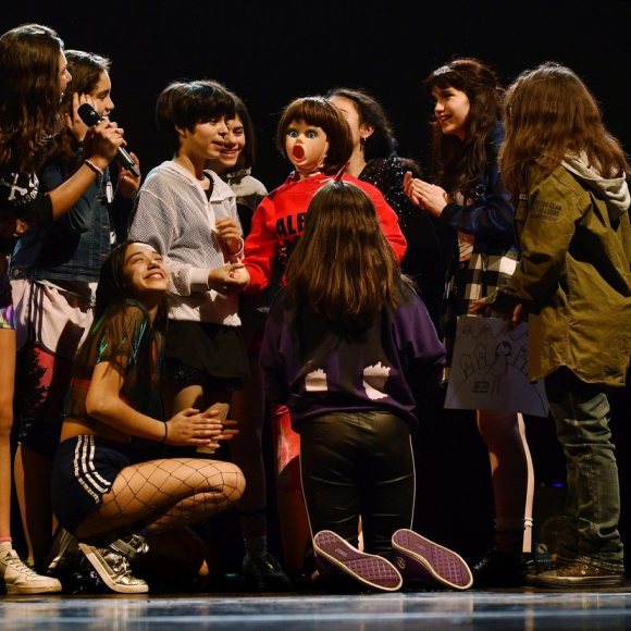 Foto de l'espectacle. Es veuen totes les adolescents actrius de l'obra al voltant d'una nina inflable vestida que estan manipulant