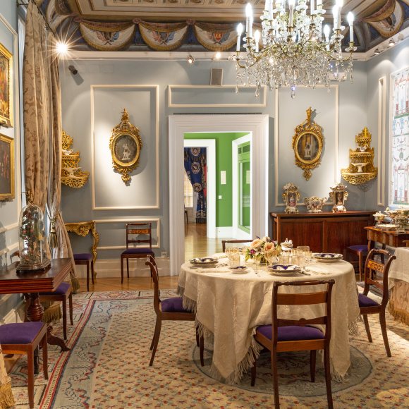 Comedor del Museo del Romanticismo: mesa con vajilla, sillas, aparador con juego de café, en una habitación con ventanas y cortinas