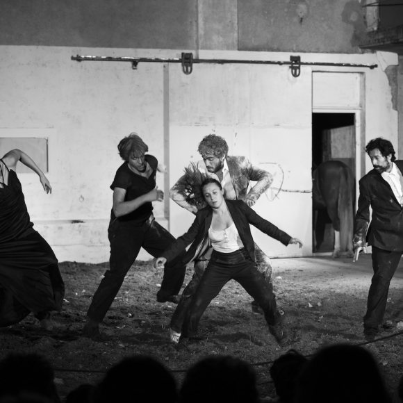 Fotografia en blanc i negre. Surten diverses persones ballant sobre un terra que sembla terra. 