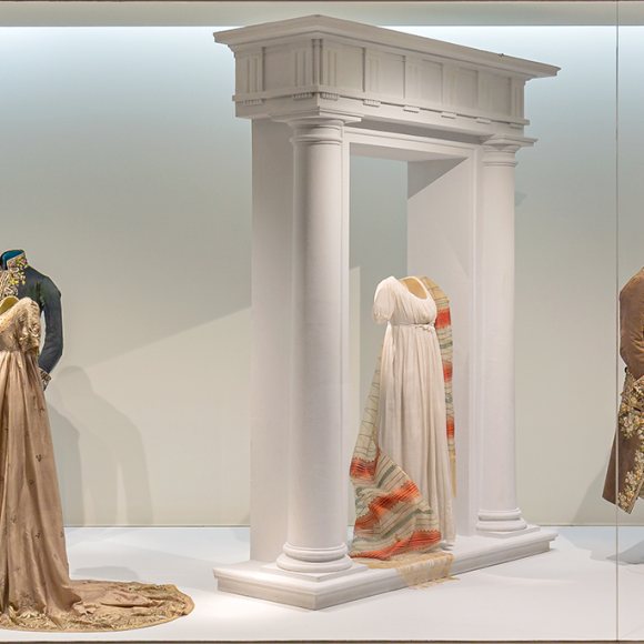 Imagen que muestra los distintos trajes y vestidos que se encuentran en la vitrina "Un nuevo clasicismo", que aborda la indumentaria de comienzos del siglo XIX. Forma parte del recorrido de la visita por la exposición permanente del Museo.